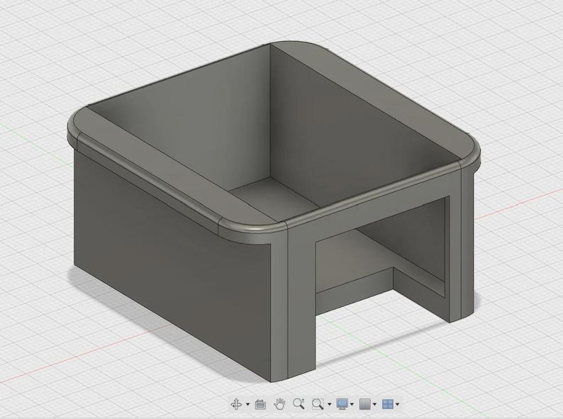 May include: A gray, box-shaped object with rounded edges and an open top. The design features a recessed base and a smooth, solid construction. The object appears to be a 3D model or a digital rendering.