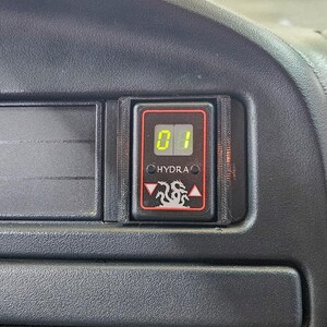 May include: A black dashboard with a digital display showing the number "01" in green. The display is framed in a black housing with the word "HYDRA" and a dragon logo. The dashboard has a textured surface.
