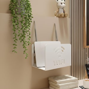May include: A white metal wall-mounted router shelf with a WiFi symbol and the word "WIFI" cut out. The shelf holds a white router with two gray antennas. A green hanging plant is visible on the left.