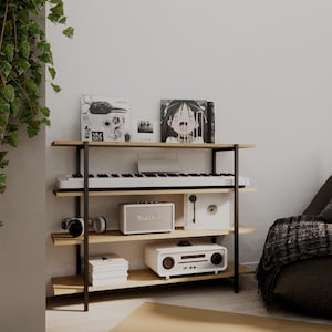 Puede incluir: Estantería de madera y metal negro que muestra equipos de música y audio. Los artículos incluyen un teclado, altavoces, auriculares y discos de vinilo. Los estantes son de madera clara.