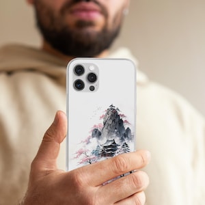 May include: A clear phone case with a Japanese landscape watercolour painting. The design features a mountain, a pagoda, cherry blossom trees, and a misty atmosphere. The case has a clear border and a camera cutout.