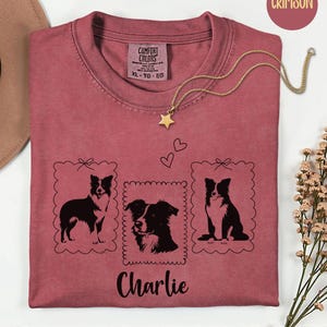 May include: Crimson-colored t-shirt with three framed dog illustrations and the name "Charlie" in black script. A gold star pendant necklace rests on the shirt. The shirt has a Comfort Colors tag.
