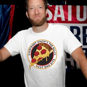 May include: A white t-shirt with a pizza slice graphic. The design includes the text "EVERYBODY KNOWS THE RULES JUST ONE BITE" in a circular format. The pizza has pepperoni and melted cheese.
