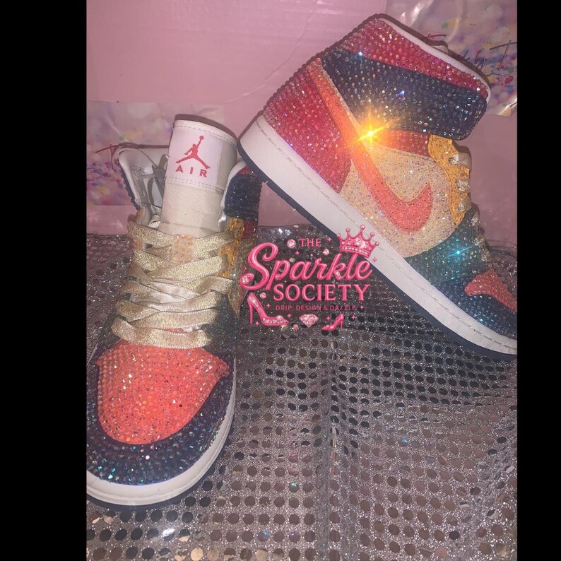 Puede incluir: Un par de zapatillas altas, muy adornadas con brillantes pedrer&iacute;a en una vibrante gama de colores. Los zapatos tienen una suela blanca, un logotipo de Nike y el texto "AIR" en la leng&uuml;eta. Los zapatos forman parte de la colecci&oacute;n "The Sparkle Society".