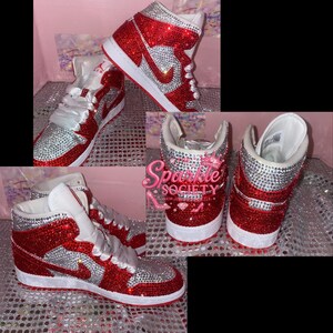 Puede incluir: Zapatillas altas rojas y plateadas con suela blanca. Las zapatillas est&aacute;n cubiertas de brillantes pedrer&iacute;a. El logo de Nike es plateado. Los cordones son de sat&eacute;n blanco. El texto "Sparkle Society" es visible.