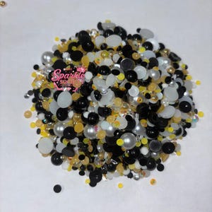 May include: A pile of assorted embellishments in black, white, silver, and yellow. The mix includes beads, pearls, and flat-backed gems. The text "Sparkle Society" is visible in the upper left corner.