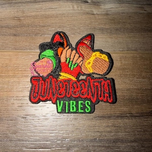 May include: Embroidered patch with the words "Juneteenth Vibes" in red and green. The patch features a design of a hand holding a hot dog and a slice of watermelon.