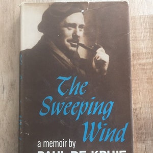 May include: A brown book cover with a black and white photo of a man with a pipe. The title of the book is "The Sweeping Wind" and the author is "Paul De Kruif".
