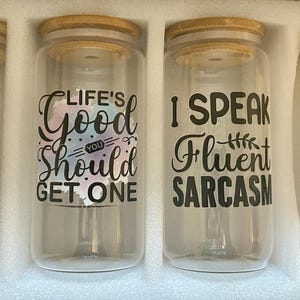 May include: Set of four clear glass tumblers with bamboo lids. Each tumbler has a different black text design: "I run on caffeine, chaos, and cuss words," "Life's good, you should get one," "I speak fluent sarcasm," and "Your opinion matters, just not to me."