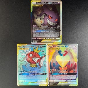 May include: Three Pokemon trading cards. The top card features Gengar and Mimikyu. The bottom left card shows Magikarp, and the bottom right card displays Latias and Latios. Each card has a unique design and text.