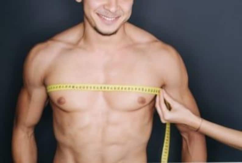 May include: A person's chest is being measured with a yellow measuring tape. The tape is held horizontally across the chest. The person is smiling. The background is a dark gray color.