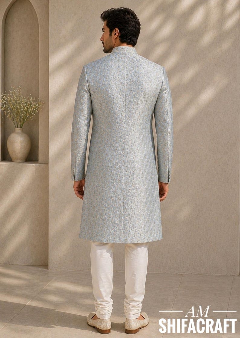 Pu&ograve; includere: Un cappotto grigio chiaro a maniche lunghe con un motivo sottile, abbinato a pantaloni bianchi. Il cappotto ha un colletto alla coreana e polsini con bottoni. Il testo "AM SHIFACRAFT" &egrave; in basso.