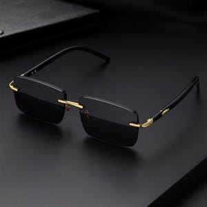 Peut inclure: Lunettes de soleil sans monture avec verres noirs rectangulaires et des accents dorés. Les branches sont noires avec des détails dorés. Les lunettes de soleil sont posées sur un fond sombre.