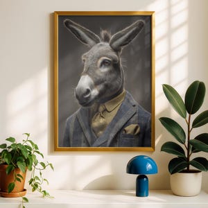 Può includere: Ritratto incorniciato di un asino con un abito a quadri blu, camicia e cravatta dorate. L'asino ha il pelo grigio e orecchie lunghe. L'opera d'arte è in una cornice dorata ed è esposta su una mensola bianca con piante e una lampada blu.