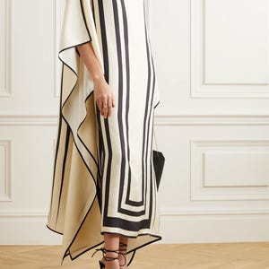 May include: A cream-colored, flowing dress with bold black vertical stripes and geometric patterns. The dress features a boat neckline and wide sleeves. Black high-heeled shoes with ankle ties complete the look. The dress is a stylish garment.