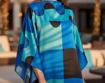 May include: A blue, teal, and black patterned caftan. The caftan features a geometric design with large semi-circles and squares. The garment has wide sleeves and a relaxed fit. The model is wearing the caftan outdoors.
