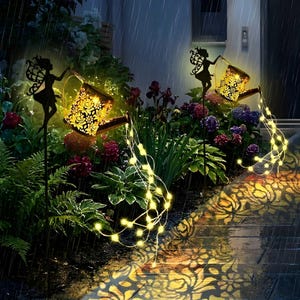 Puede incluir: Luces solares decorativas para jardín con una silueta de hada sosteniendo una regadera. Las regaderas tienen un diseño floral y emiten una luz cálida. Las luces proyectan un patrón floral en el suelo. Las luces están en un jardín.
