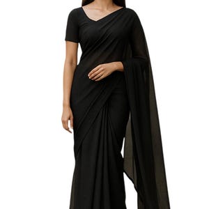 Puede incluir: Un sari negro liso con una blusa a juego de manga corta. El sari está elegantemente drapeado, con un pallu fluido. La tela parece ligera y semitransparente, creando una silueta elegante. Adecuado para eventos formales.