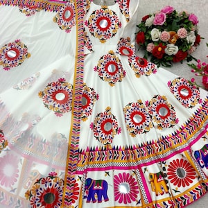May include: White dress with colorful floral and mirror embellishments. The dress features a round neckline and short sleeves. The skirt has a vibrant border with elephant and floral designs. A matching white scarf is included.