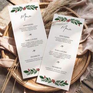 Könnte beinhalten: Zwei vertikale weiße Menükarten mit einer weihnachtlichen Illustration aus grünen Stechpalmenblättern und roten Beeren oben und unten. Der Text enthält Überschriften für Appetizers, Main Course und Desserts mit in Schwarz gedruckten Speiselisten.