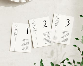 Könnte beinhalten: Drei weiße Tischkarten mit schwarzem Text. Jede Karte hat das Wort "TABLE" vertikal links und eine Zahl (1, 2 oder 3) rechts oben. Jede Karte listet Namen unter der Zahl auf.