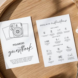 May include: Two white cards with black text and illustrations. One card reads "POLAROID guestbook" with instructions. The other card has "camera instructions" with diagrams. The guestbook card includes a Polaroid camera illustration.