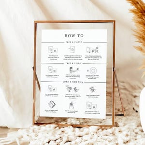 May include: A white instructional sign in a copper-colored metal frame with glass panels. The sign features black text and line drawings titled HOW TO, with sections for taking a photo, taking a selfie, and loading new film for a camera.