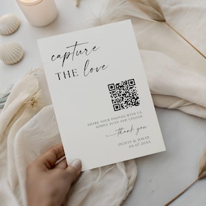 May include: A cream-colored wedding sign with the words "capture the love" in elegant script. It includes a QR code and the text "Share your photos with us. Simply scan and upload. Thank you, Olivia & David 05.07.20XX."