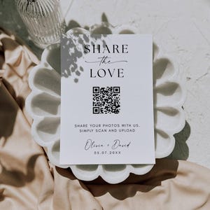 May include: A white rectangular sign with black text reading SHARE the LOVE, a QR code, and the text SHARE YOUR PHOTOS WITH US. SIMPLY SCAN AND UPLOAD, followed by the names Olivia + David and the date 05.07.20XX in a serif and script font.