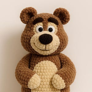 May include: A handmade brown and tan crochet bear with a friendly expression. The bear has a light tan muzzle, belly, and paw pads, with dark brown accents on the nose, eyes, and ears. The bear's arms are positioned in front of its body.