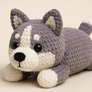 May include: A plush crochet husky dog in gray and white, lying down. The amigurumi dog has black eyes and a black nose. The text "Amigurumi Husky Plush Crochet" is at the bottom of the image.