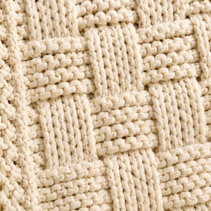 May include: Close-up of a cream-colored woven textile with a basketweave pattern. The texture is thick and the weave is tight, creating a sturdy and durable appearance. The neutral color makes it versatile for various uses.