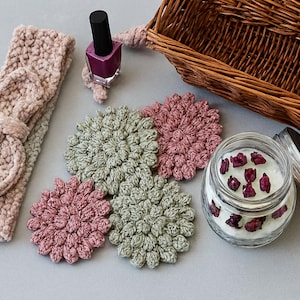 May include: A collection of handmade items including a crochet headband with a bow, flower-shaped coasters in pink and green, a jar candle with rose petals, and a nail polish bottle. A woven basket is also present.