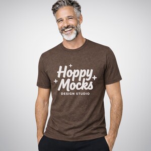 Può includere: Una maglietta marrone con la scritta "Hoppy + Mocks DESIGN STUDIO" in bianco. La maglietta è a maniche corte e ha uno scollo tondo. La persona che indossa la maglietta sta sorridendo.