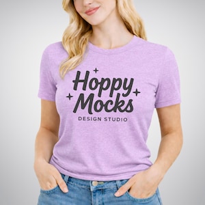Puede incluir: Una camiseta de color lila claro con el texto "Hoppy Mocks DESIGN STUDIO" en negro. La camiseta de manga corta está hecha de un tejido suave. La persona lleva vaqueros azules.
