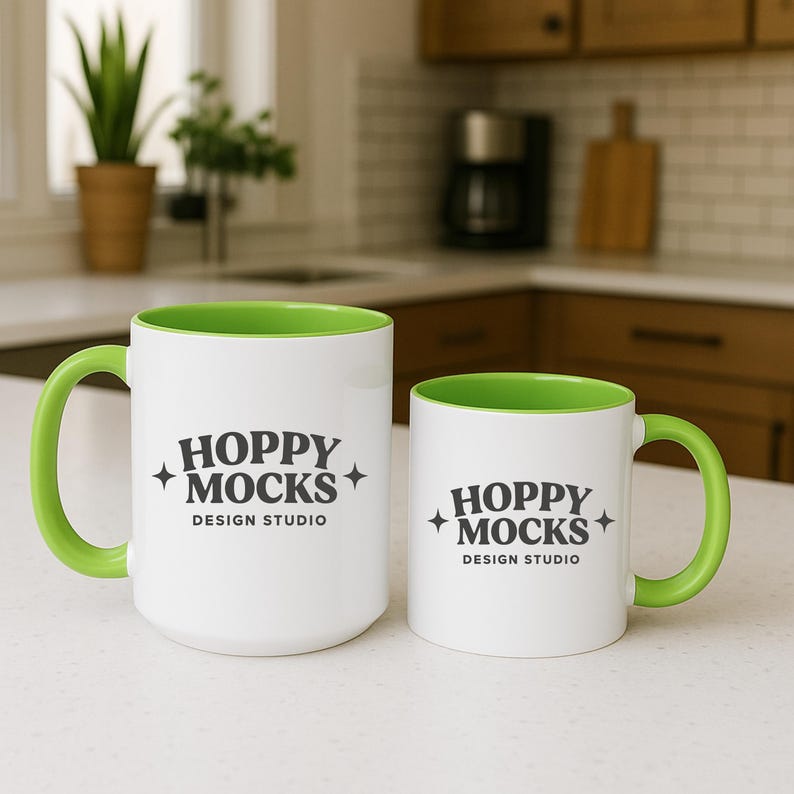May include: Two white ceramic mugs with green interiors and handles. The mugs have the text "HOPPY MOCKS DESIGN STUDIO" printed in black. One mug is larger than the other.