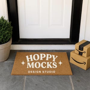 Puede incluir: Felpudo rectangular de fibra natural con las palabras "HOPPY MOCKS DESIGN STUDIO" en blanco. Dos cajas de Amazon apiladas a la derecha de la alfombra. Una planta en maceta a la izquierda.