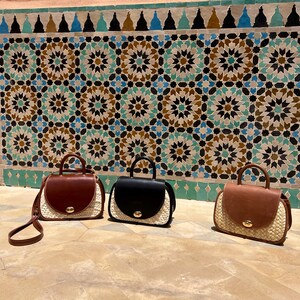 May include: Three handbags with a top handle and a flap closure. The bags have a woven straw base and a leather top in brown and black. The bags are displayed in front of a decorative tile wall.