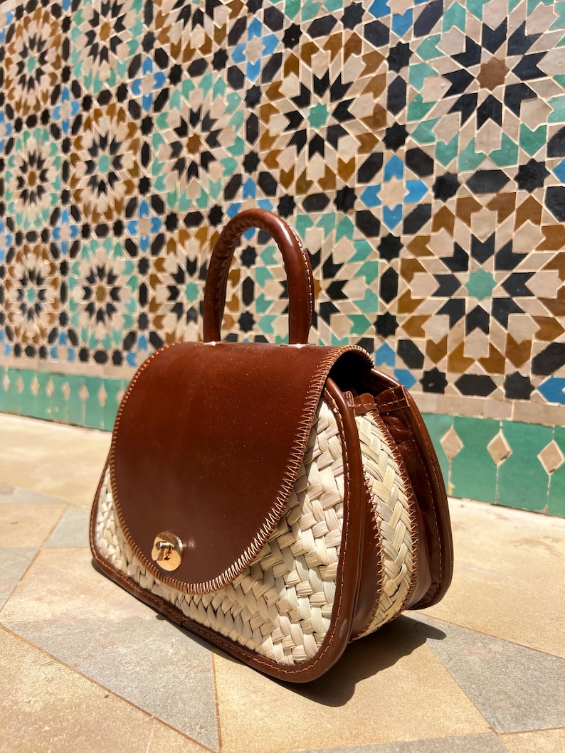 May include: A brown leather and woven straw handbag with a top handle and a gold-colored clasp. The bag has a rounded shape and a woven straw body with brown leather accents.