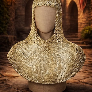 Könnte beinhalten: Ein goldfarbener Kettenhaubenkragen, präsentiert auf einem Schaufensterkopf. Die Kettenhaube besteht aus kleinen, ineinandergreifenden Metallringen, die eine flexible, schützende Abdeckung bilden. Der Kragen bedeckt Kopf, Hals und Schultern. Der Hintergrund zeigt eine Steinstruktur.