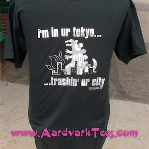 May include: Black t-shirt with a white graphic of a monster destroying a city. The text on the shirt reads "i'm in ur tokyo... trashin' ur city".