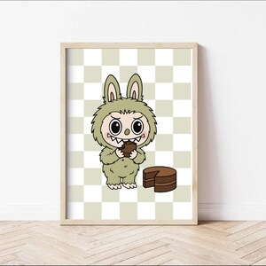 May include: A framed print featuring a cartoon monster in a green bunny suit, eating a piece of chocolate cake. The background is a checkered pattern in light green and white. The artwork is whimsical and playful.