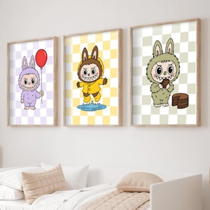 May include: Three framed art prints featuring cartoon characters in bunny costumes. One holds a red balloon, another is in a yellow raincoat, and the third holds a slice of cake. Each character is set against a checkered background.