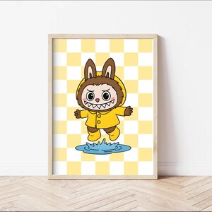 May include: A framed cartoon print of a creature in a yellow raincoat and boots, with bunny ears, jumping over a puddle. The background is a yellow and white checkered pattern. The artwork is in a wooden frame.
