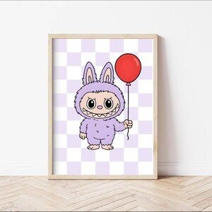 May include: A framed print featuring a cartoon monster in a purple bunny suit holding a red balloon. The monster has a wide grin and large eyes. The background is a checkered pattern of light purple and white.
