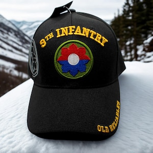 May include: Black baseball cap with embroidered text and a colorful patch. The cap features the words "9th Infantry" in yellow, and "Old Reliables" in yellow. The patch has a red, blue, and white floral design.