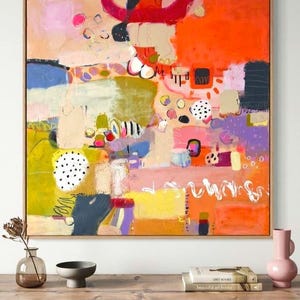 May include: A large square abstract painting in a light wood frame featuring vibrant blocks of orange, pink, yellow, purple, and blue. The composition includes various hand-drawn shapes, black and white polka dots, and white scribbled lines.