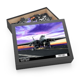 May include: A 16x20 inch puzzle box with a dramatic image of a jet fighter on a runway at sunset. The box is open, revealing some puzzle pieces. The box text reads "16x20 Puzzle 500 pcs Ages 9+".