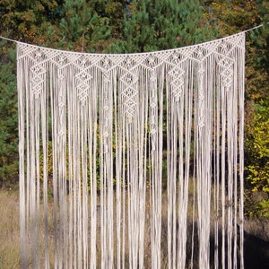 May include: A white macrame curtain backdrop with a geometric pattern, hanging in a forest setting.