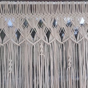 May include: A white macrame wall hanging with a geometric pattern. The hanging is made of thick cotton cord and has a fringe at the bottom.